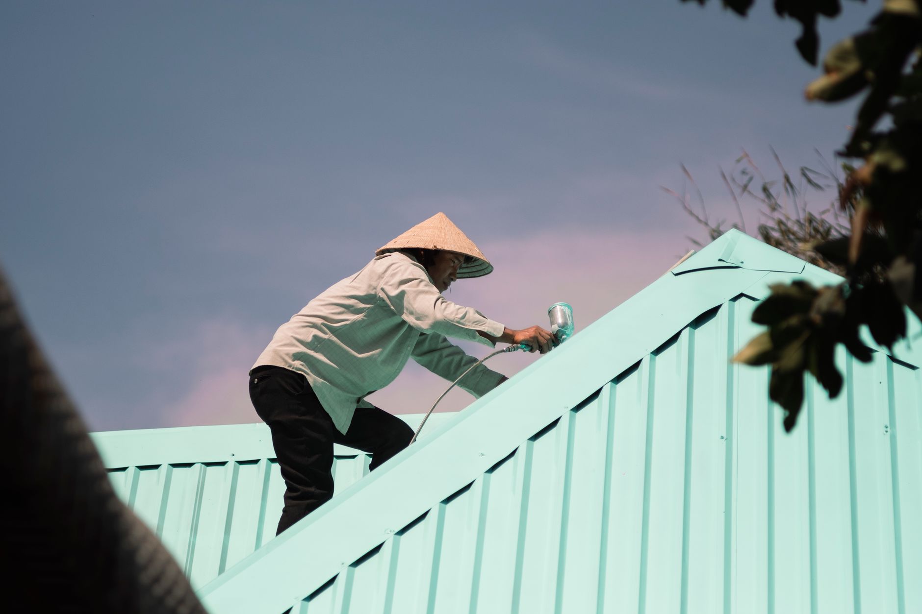 Man in conical hat paints a rooftop, engaging in outdoor work. Low angle view in Torrance, CA